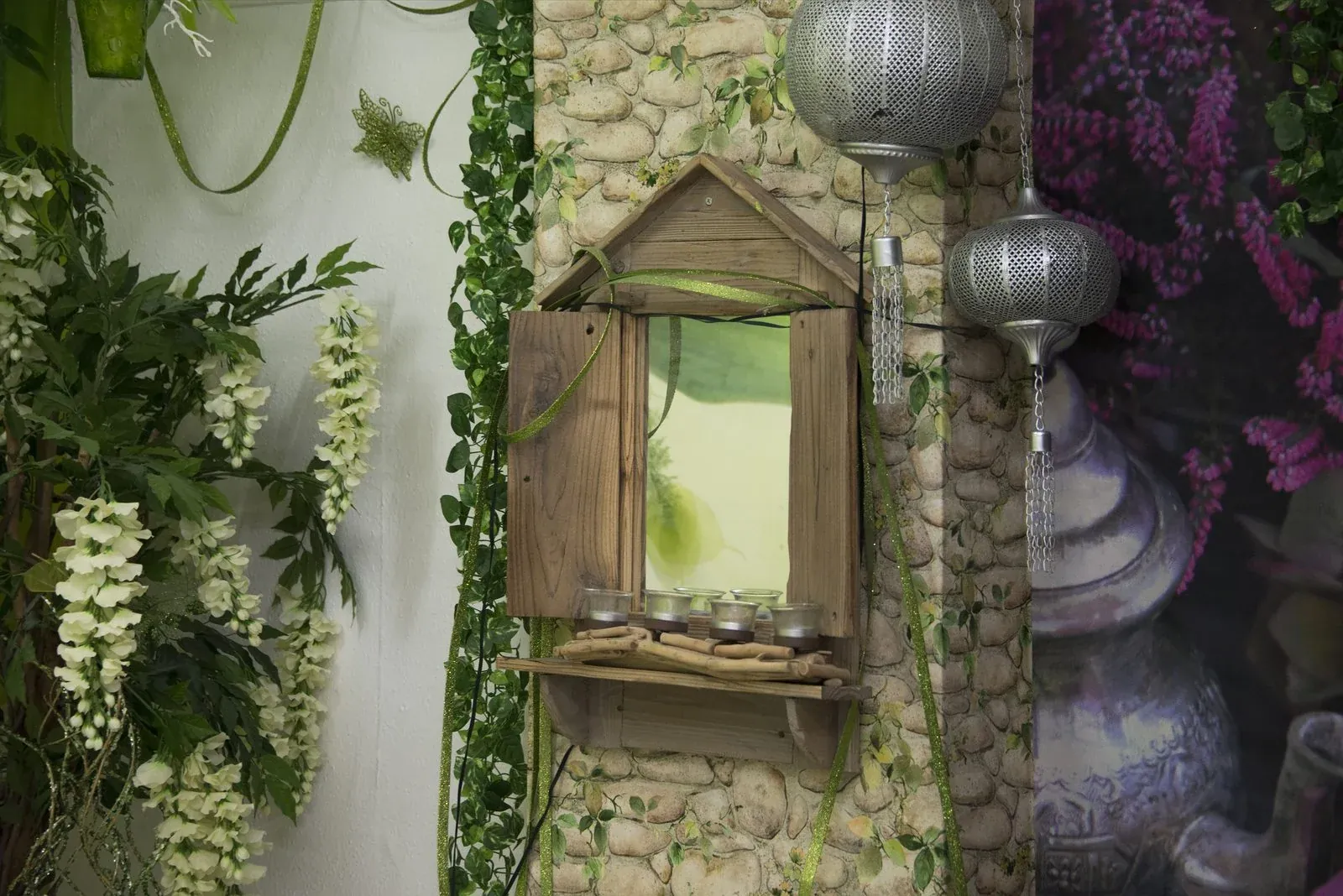 Detail of the CoLaz Hounslow relaxation room with a rustic wooden mirror on a stone-effect wall, hanging flowers and Moroccan lanterns
