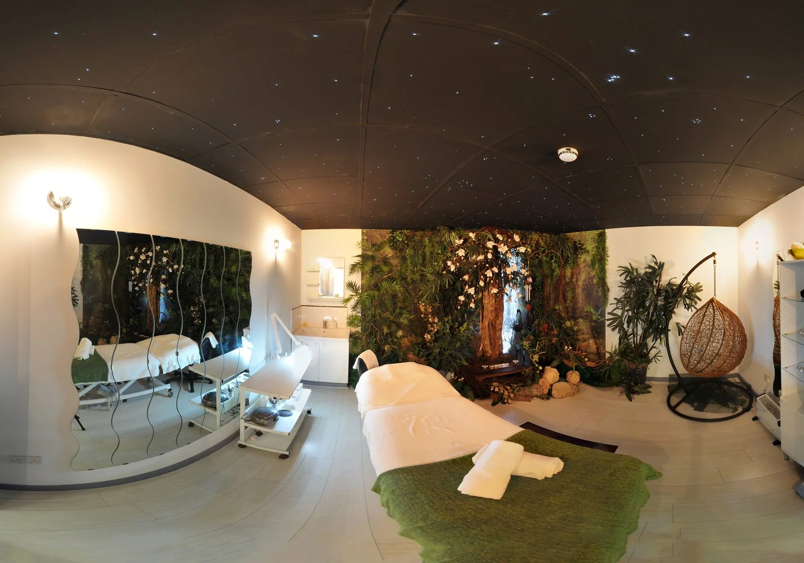 Spa-themed treatment room at the CoLaz Hounslow clinic with a starry-night ceiling, lush plant wall and a treatment bed alongside a rattan hanging chair