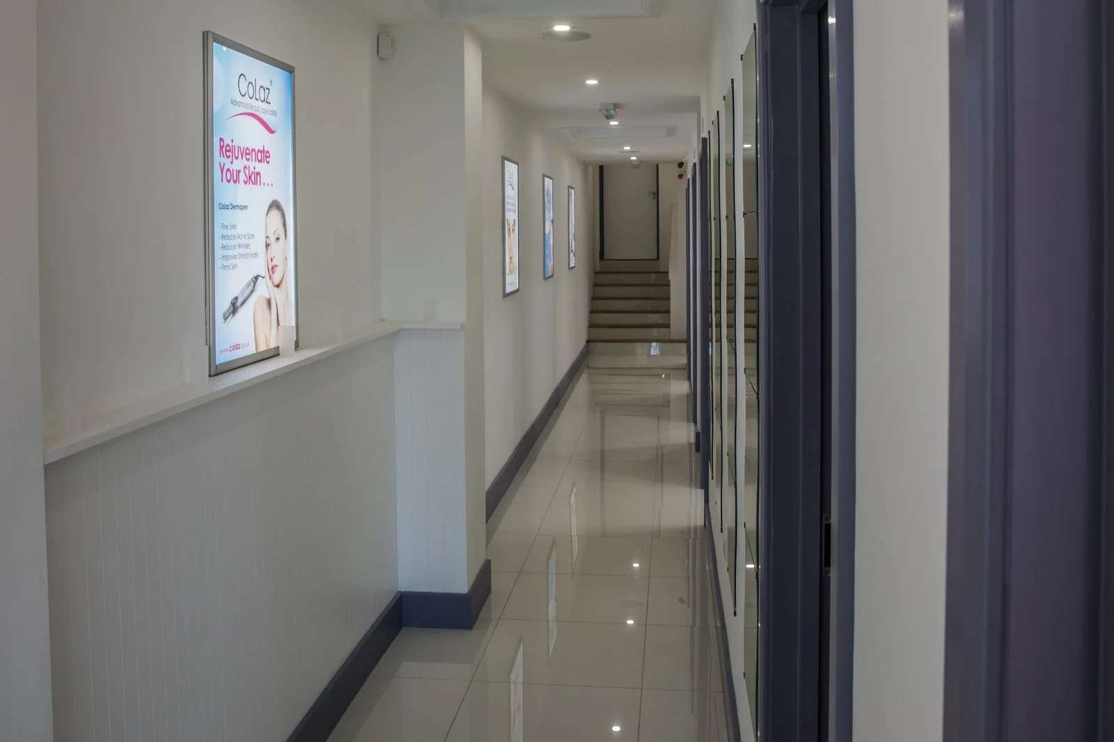Bright corridor inside the CoLaz Wembley clinic leading to private treatment rooms, with Dermapen treatment posters along the wall
