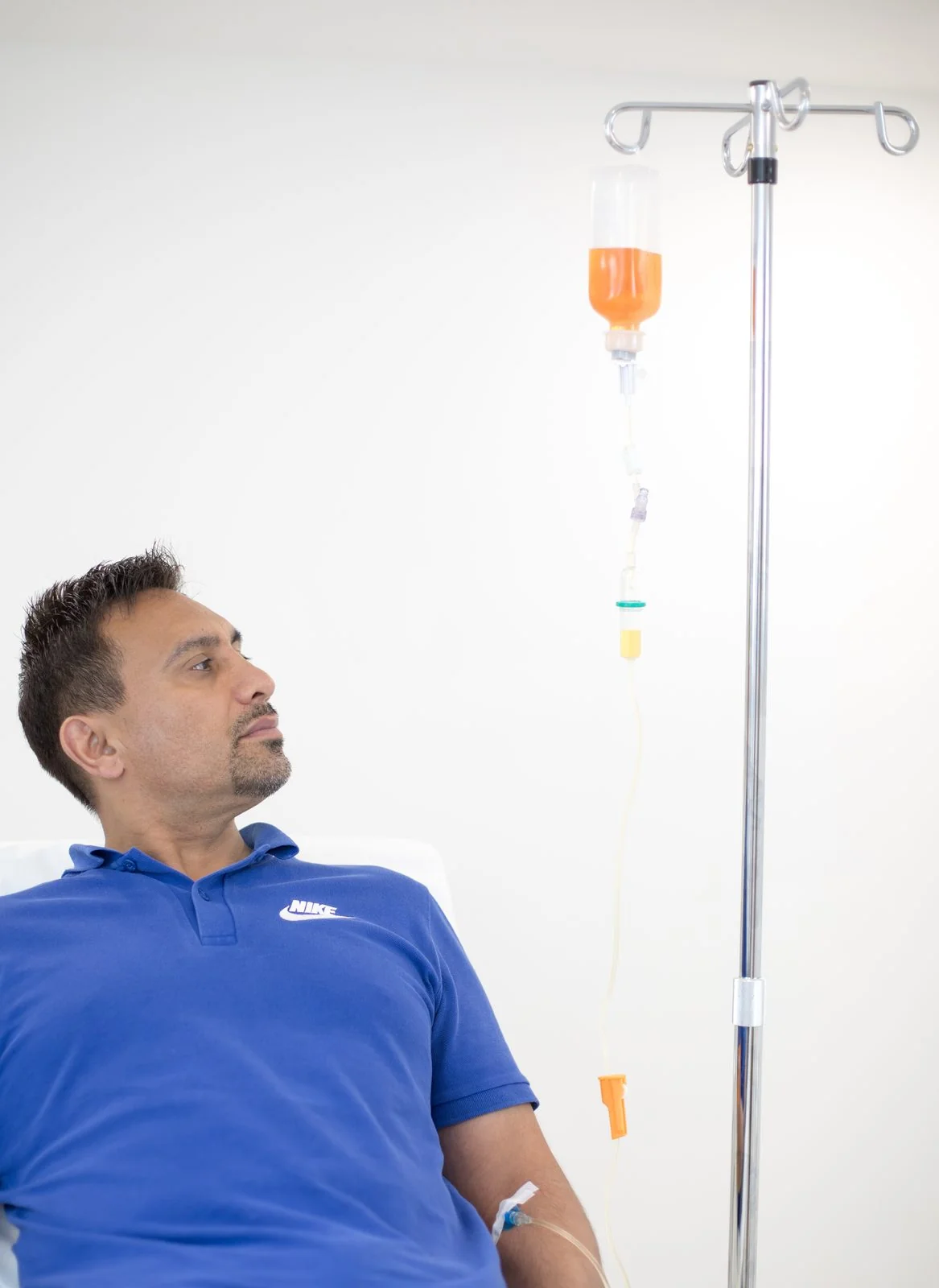 Male patient seated comfortably in the CoLaz Ealing clinic mid-IV infusion, with the prepared vitamin blend running on a stand beside him