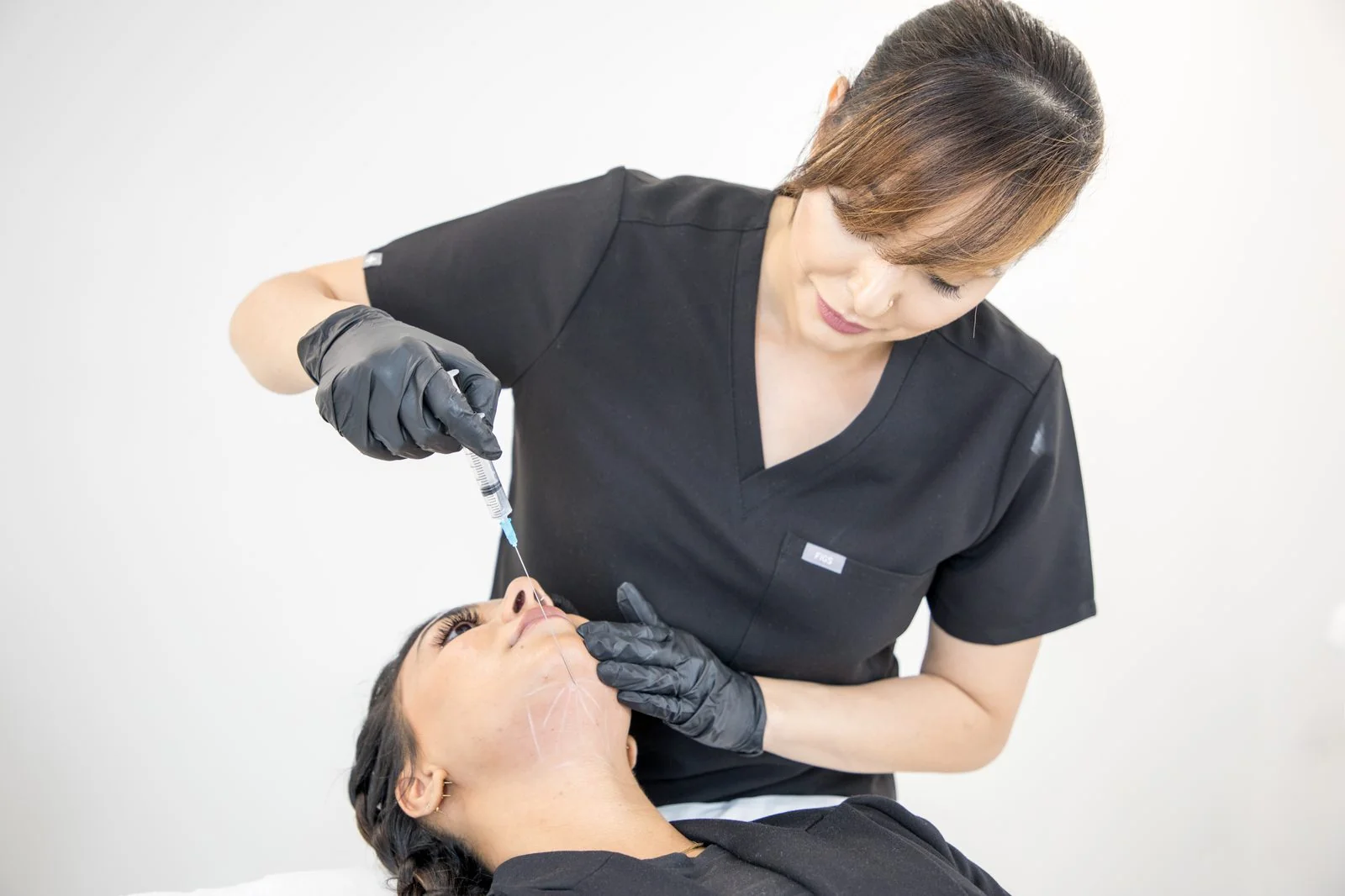 CoLaz qualified clinician at the Ealing clinic delivering a Lemon Bottle fat-dissolving injection along a patient's jawline to refine the submental fat under the chin