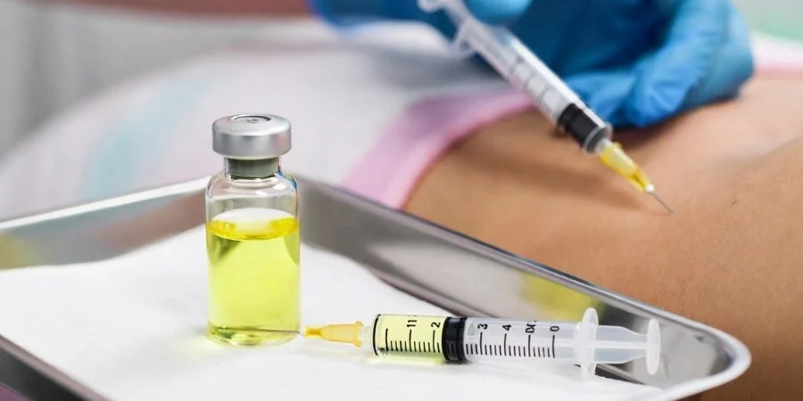 Lemon Bottle vial of riboflavin, lecithin and bromelain solution on a stainless treatment tray, with a syringe being administered to a body area in the background