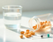 Glass of water, spilled vitamin pills, and a syringe on a white countertop